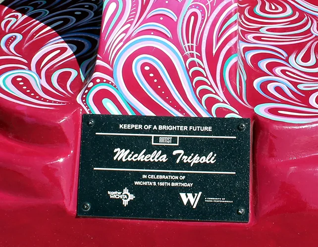A close-up of the plaque which reads: Keeper of a Brighter Future, artist Michella Tripoli, in celebration of Wichita's 150th birthday. There are logos for the organizations Together Wichita and W.