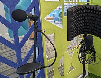 One microphone on a stand with a pop filter and another microphone on a stand with an isolation shield